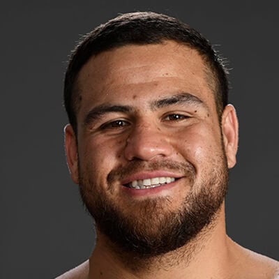 Portrait of a smiling man with short dark hair and a beard, against a gray background.