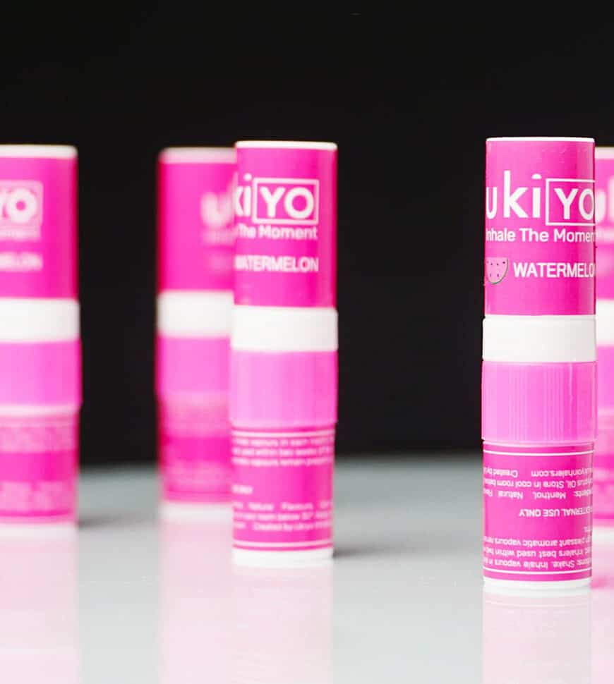 Four pink yoyo watermelon lip balms in focus in the foreground against a blurred background.