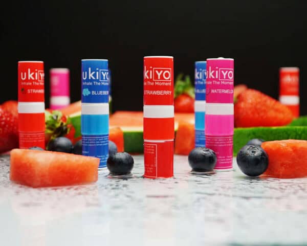 Several Mixed Twelve Pack inhaler tubes arranged with fresh strawberries, blueberries, and watermelon slices on a dark surface.