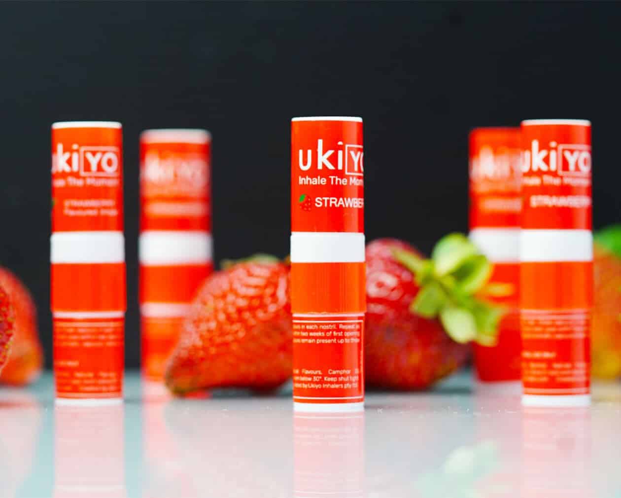 Several red Strawberry Twelve Pack tubes labeled "ukiyo" are displayed with whole strawberries in the background on a reflective surface.