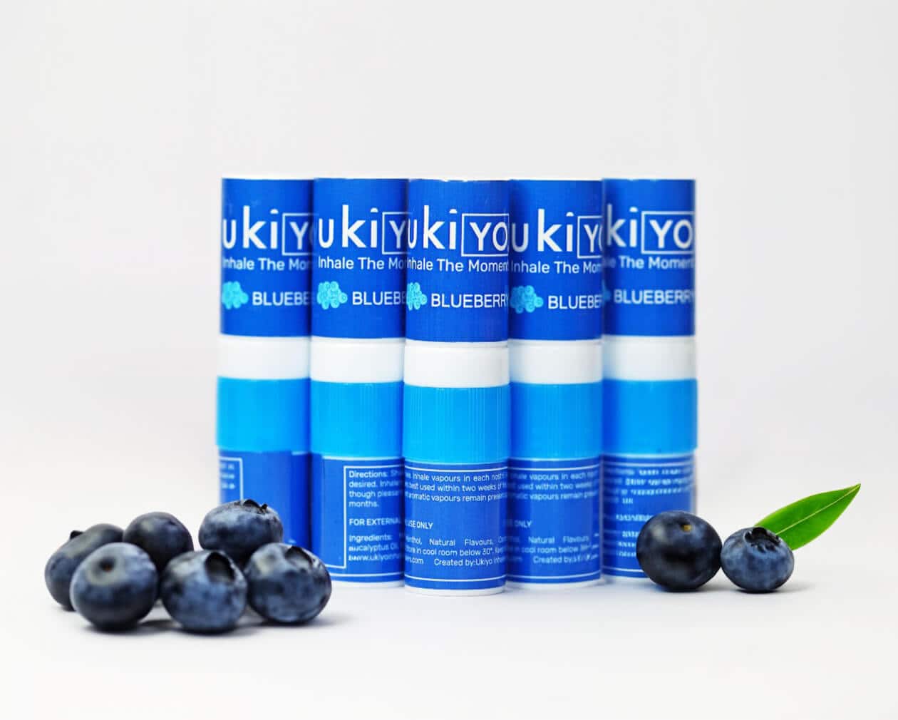 Five blue inhalers labeled "yukiYO BLUEBERRY" stand upright behind a few fresh blueberries and a green leaf on a white surface.