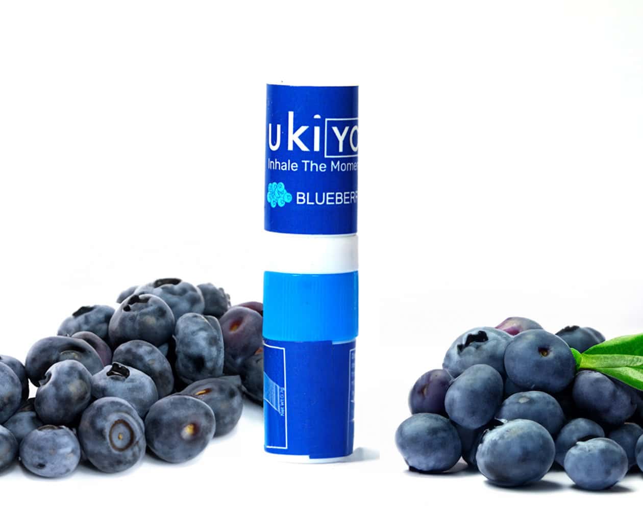 Inhaler with the label "Ukiyo" and "Blueberry" stands upright, surrounded by scattered blueberries on a white surface and background.